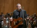 Artysta z gitarą i mikrofonem na scenie podczas koncertu Męskie Granie w Poznaniu.
