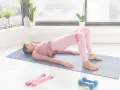 Femme faisant un pont avec une bande de résistance pour comment muscler les fessiers. Haltères et bandes roses à proximité.