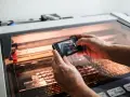 Hands hold a phone, capturing a laser cutter working on intricate acrylic projects.
