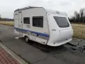 Biała przyczepa kempingowa Hobby 400 de luxe easy z niebieskimi pasami, gotowa na wakacyjne podróże.