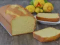 Un soffice plumcake al limone, appena sfornato, con una fetta su un piattino bianco e fiori gialli sullo sfondo.