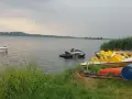Na jeziorze Paczkowskim pływa motorówka i skutery wodne. Na brzegu czekają rowery wodne i kajaki.