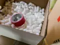 Pudełko z wypełnieniem styropianowym i czerwoną taśmą klejącą.