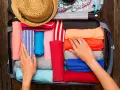 Ręce układają kolorowe ubrania w walizce. Słomkowy kapelusz i wzorzysty strój kąpielowy czekają na podróż. To gotowy bagaż na wakacje.