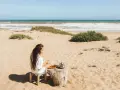 Kobieta pije herbatę na piaszczystej plaży, delektując się widokiem na turkusowe tunezyjskie morze.