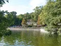 Grüne Bäume säumen den Schlachtensee Berlin, wo Menschen auf der Terrasse eines Restaurants sitzen.