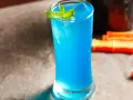 Niebieski gin z tonikiem i blue curacao, ozdobiony miętą, wygląda orzeźwiająco.