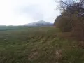 Mglisty poranek nad polami, w oddali majaczy ostrzyca proboszczowicka. Jesienne drzewa szumią przy ścieżce.