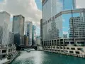 Chicago's iconic skyline along the river, with the Trump Tower reflecting the clouds. A boat glides by, making you wonder, is Chicago worth visiting?