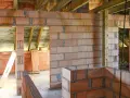 Budowa domu w toku. Ściany z pustaków ceramicznych, widoczne drewniane belki stropowe. Trwa murowanie na piankę.