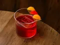 Klasyczny negroni przepis: czerwony koktajl z lodem i pomarańczową dekoracją na drewnianym blacie.