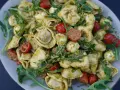 Ein köstlicher Tortellini-Salat mit Pesto, Kirschtomaten und Mozzarella-Kugeln, garniert mit Rucola.