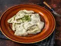 Talerz pełen pierogów, które przypominają o tradycji i pytają skąd pochodzą pierogi. Zioła dodają świeżości.