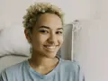 Uśmiechnięta młoda kobieta z kręconymi blond włosami i kolczykiem w nosie (septum piercing).