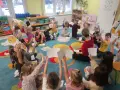 Wychowawca prowadzi zajęcia z dziećmi, które trzymają w rękach rysunki buziek wyrażających różne emocje.