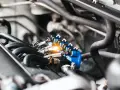 Close-up of a car's engine, focusing on a blue fuel injector rail with glowing orange light. This image might help you understand the fuel injector replacement cost.