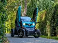 Niebieski Renault Twizy z otwartymi drzwiami stoi na ścieżce wśród zieleni.