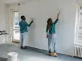Pareja pintando una pared blanca, renovando su hogar. El hombre y la mujer usan rodillos para pintar sobre lacado, transformando el espacio.
