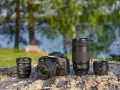 Aparat Canon EOS 90D z obiektywami 10-18mm, 70-300mm i 50mm na kamieniu nad jeziorem.