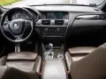 Wnętrze BMW X3 z brązową skórzaną tapicerką i drewnianymi wstawkami. Kierownica, deska rozdzielcza i nawigacja. Wiele osób szuka bmw x3 opinie, by poznać ten model.
