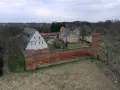 Zamek Kiszewski, z ceglanymi murami i wieżą, otoczony zielenią i drzewami.