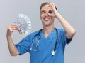 Giovane oss con stetoscopio e banconote in mano, fa un gesto con l'occhio, mostrando soddisfazione per il suo oss lavoro.