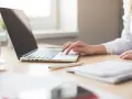 Mano su laptop, penna e quaderno. Ricerca su quanto guadagna un traduttore.