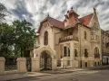 Elegancka willa w stylu art nouveau z bogatymi zdobieniami, kutą bramą i ozdobnym balkonem.