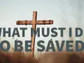 A wooden cross stands in a field of dry grass. Text reads: "WHAT MUST I DO TO BE SAVED?" This image explores the question of how to get to heaven.