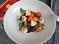 Czarny makaron z krewetkami, pomidorkami i bazylią na talerzu. Obok widoczna paczka spaghetti nero di seppia.