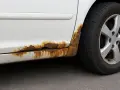 Rostfläckar på en vit bil, där billack har börjat lossna och blottlägga metallen. Dags att ta bort billack och rost.