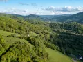 Zielone wzgórza Beskidu Śląskiego, pokryte lasami i polanami, z widocznymi domami i drogą.
