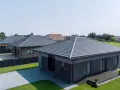 Nowoczesne domy z szarym, czterospadowym dachem, otoczone zielenią i podjazdami z kostki brukowej.