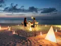 Romantyczna kolacja na plaży. Para świętuje rocznicę ślubu przy blasku świec i latarni, w otoczeniu oceanu i zachodzącego słońca.