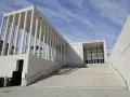 Moderne berlin architektur: James-Simon-Galerie mit langer Treppe und Säulengang vor blauem Himmel.