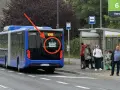 Niebieski autobus przegubowy z napisem "PRZEJAZD TESTOWY" na tyle, stoi przy przystanku autobusowym.