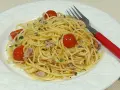 Espaguetis al ajillo con tomates cherry y atún, servidos en plato blanco con tenedor rojo.