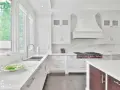 Cocina blanca moderna con encimeras de mármol, campana extractora y estufa profesional.