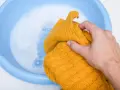 Ręka zanurza w wodzie z pianą żółty, sfilcowany sweter.