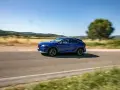 Niebieski Lexus 450h pędzi po wiejskiej drodze, otoczony zielenią i wzgórzami.