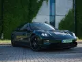 Elegancki, ciemnozielony Porsche Taycan na tle zielonej ściany z bluszczu. Sprawdź aktualną porsche taycan cena i możliwości tego elektrycznego cudu.