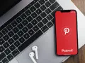 Telefon z aplikacją Pinterest obok klawiatury laptopa i słuchawek.