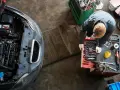 Meccanico con guanti bianchi esamina un motore sbiellato, circondato da attrezzi e un'auto con il cofano aperto.