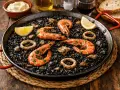 Paella de arroz negro con gambas, calamares y limón en una sartén.