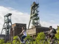 Zwei Radfahrer genießen die Landschaft am ehemaligen Bergwerk Ewald. Die imposanten Fördertürme stehen im Hintergrund.