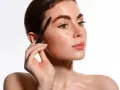 Une femme applique un mascara pour un maquillage des yeux parfait. Ses sourcils sont brossés et ses cils sont mis en valeur.