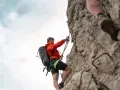 Kletterin im orangefarbenen Anzug sichert sich am Drahtseil des Alpspitz Klettersteigs. Ein spannendes Abenteuer in den Bergen.
