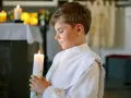 Chłopiec w białej albie trzyma zapaloną świecę. To ważny moment, zastanawiasz się, ile trwa komunia?