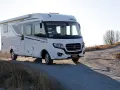 Vit husbil, en Rapido M66, parkerad på en grusväg med torrt gräs och träd i bakgrunden.