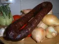 Wędzona kiełbasa z dzika na talerzu z warzywami: cebulą, pomidorami, kalarepą i czosnkiem.